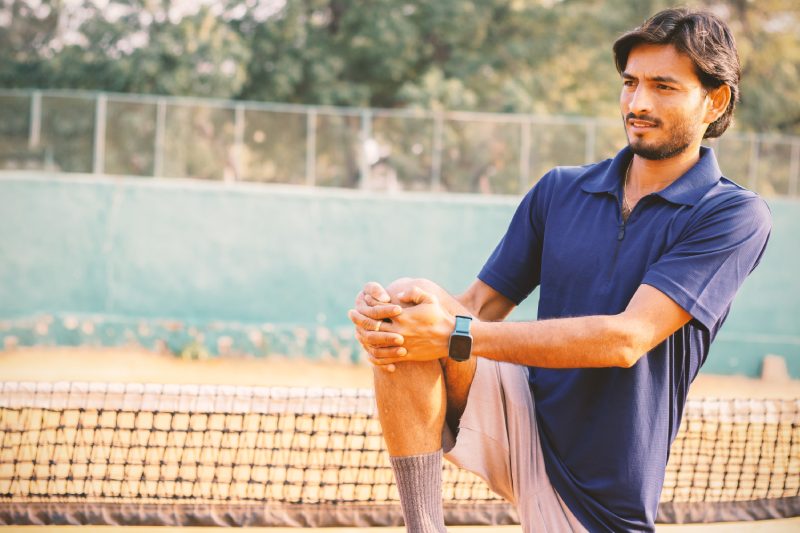 Young tennis player stretches legs before playing at tennis court - concept of warming up before playing any sports.