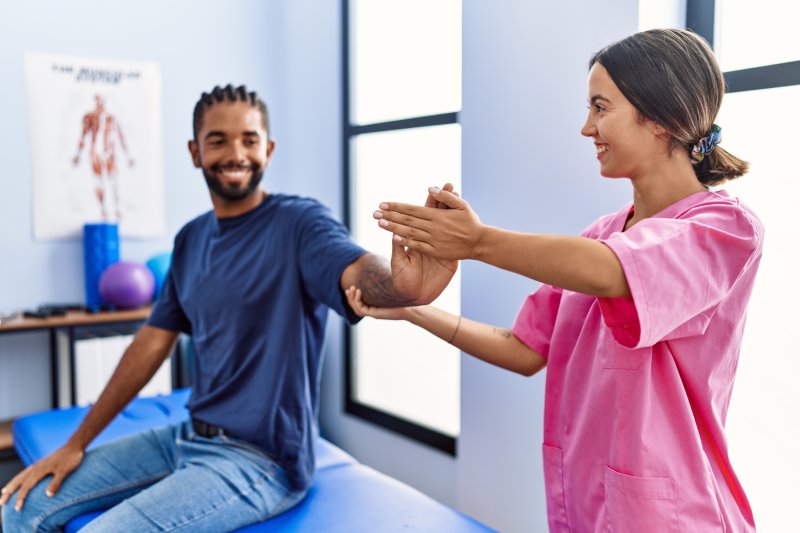 Man and woman wearing physiotherapist uniform having rehab session stretching arm at physiotherpy clinic