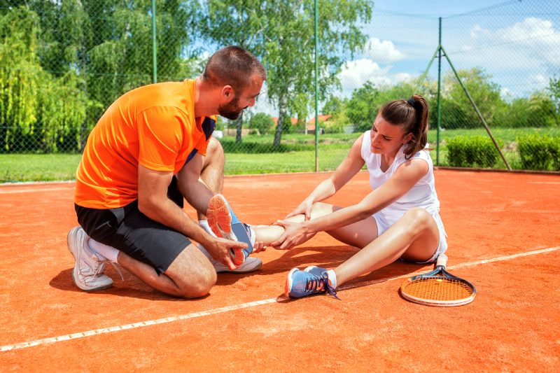 Injured girl on the tennis court with her coach trying to help her