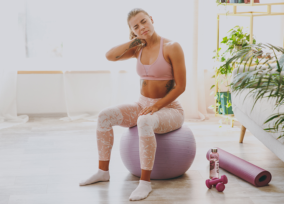 Woman sitting on top of a yoga ball, holding her neck in discomfort due to neck pain