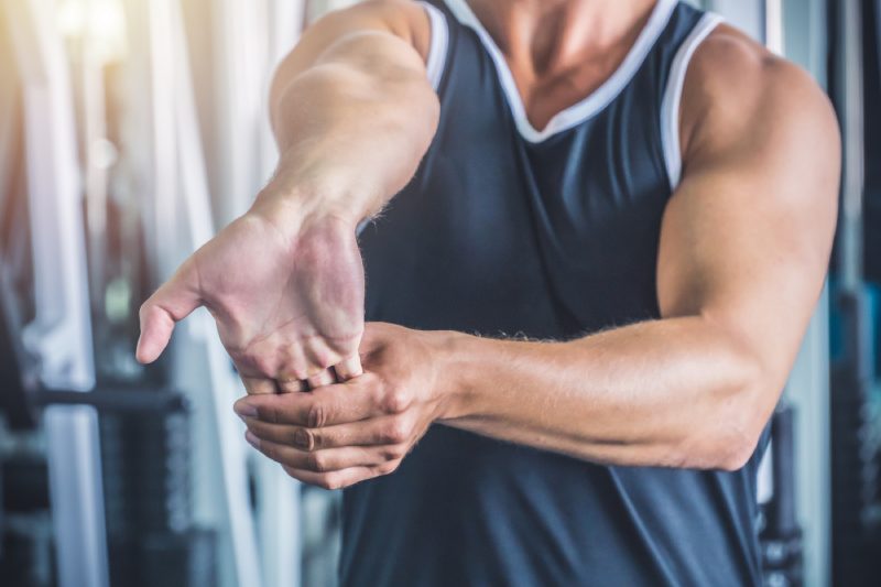 Man stretching his right hand in the gym. Workout preparation warm-up concept.