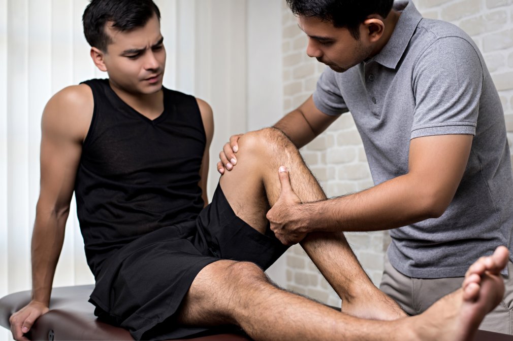 Therapist treating injured knee of handsome athlete male patient - sport physical therapy concept
