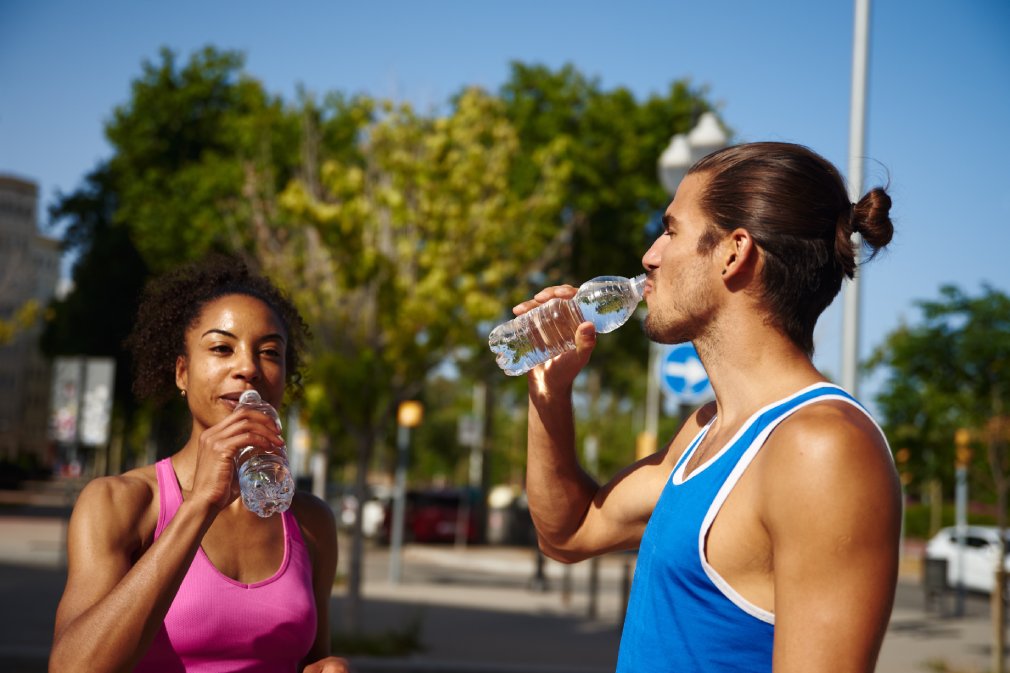 Fit young couple drinking water while taking a break from working out outdoors in the city